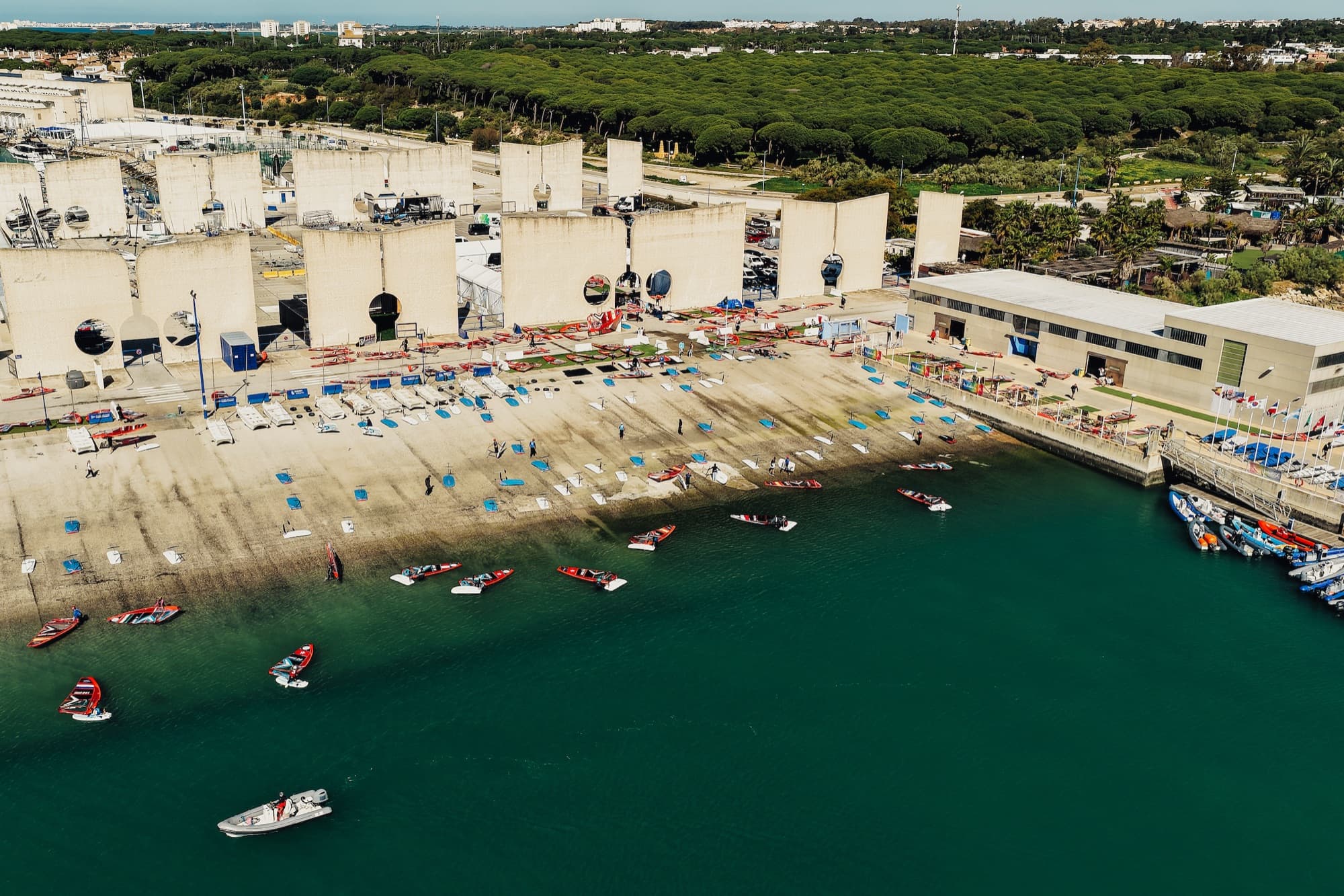 Luftaufnahme des Boat Parks am Wasser, Boards und Segel am Ufer, Begleitboote davor