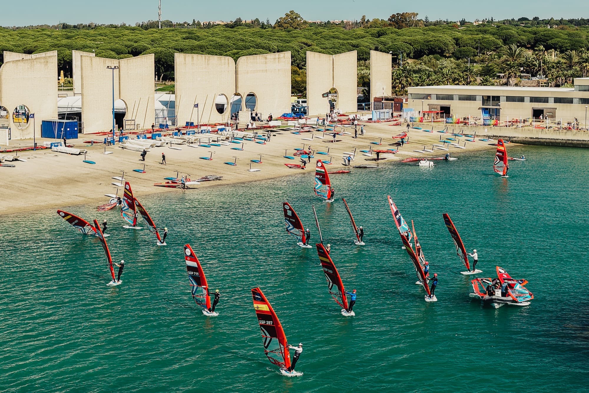 Blick von oben auf den Strand, mehrere Fahrer starten ins Wasser, weitere Boards liegen bereit