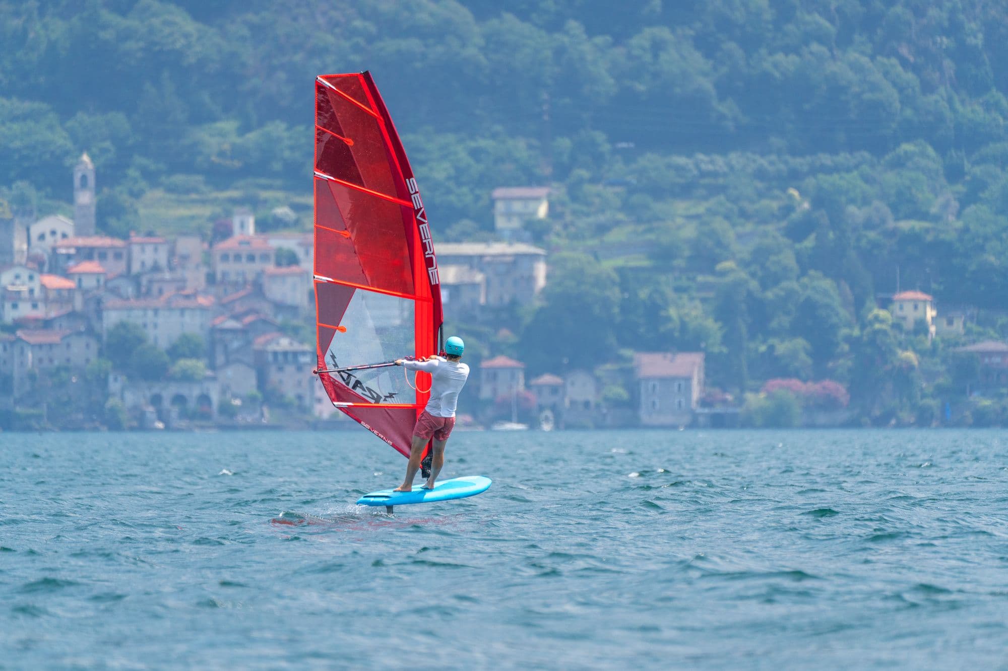 Windsurf-Foiling mit rotem Segel vor dem Dorf Cremia