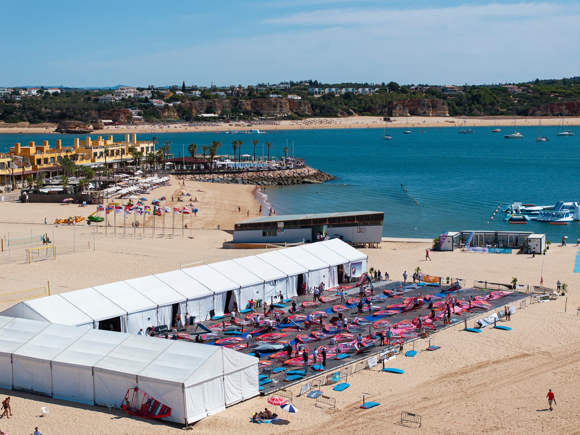 Blick über den Strand zum Zeltlager der Regatta, dahinter die Bucht und die Felsküste