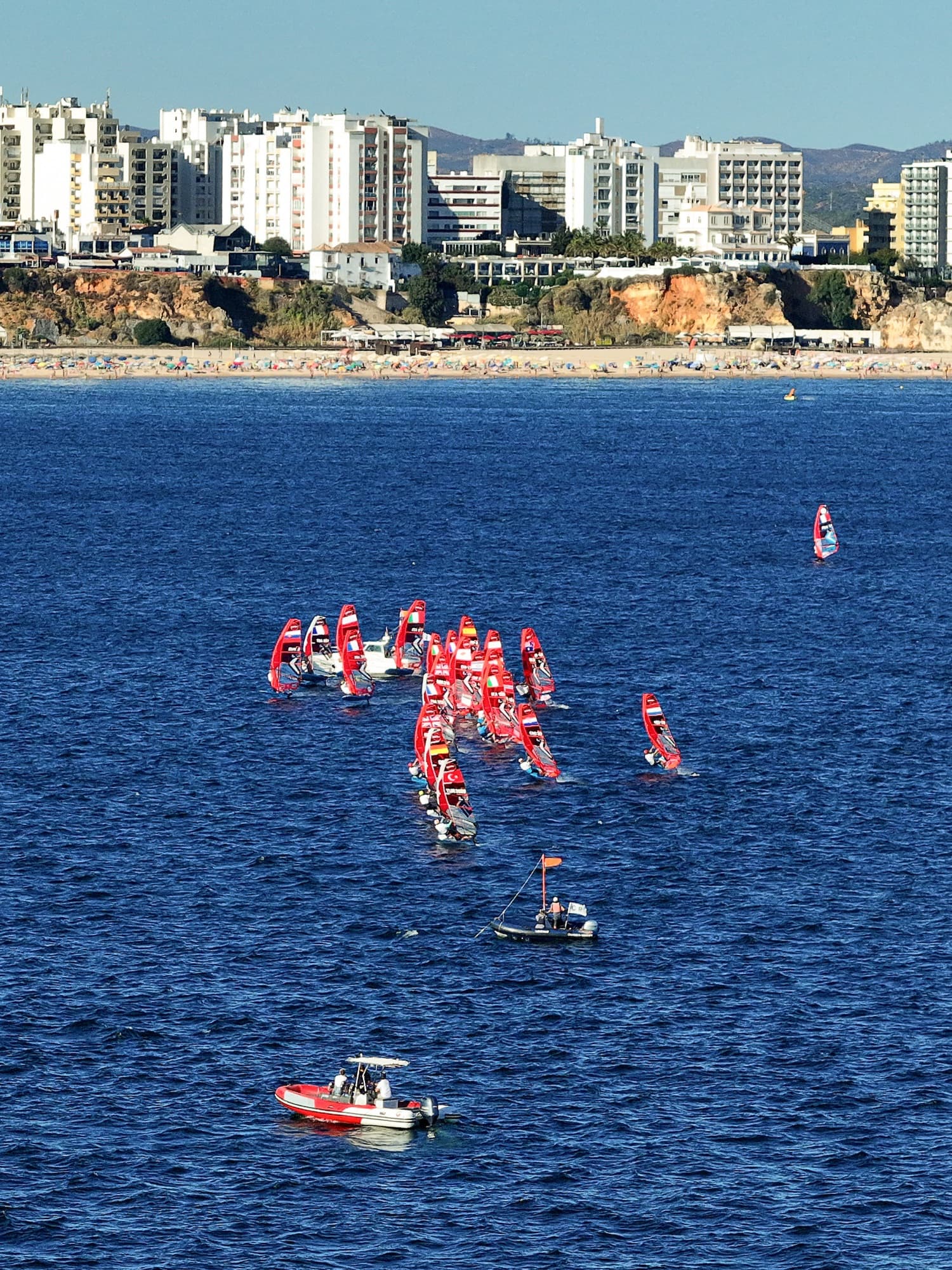 Hochformat von der Klippe: eine Gruppe Fahrer und zwei Begleitboote auf dem tiefblauen Wasser