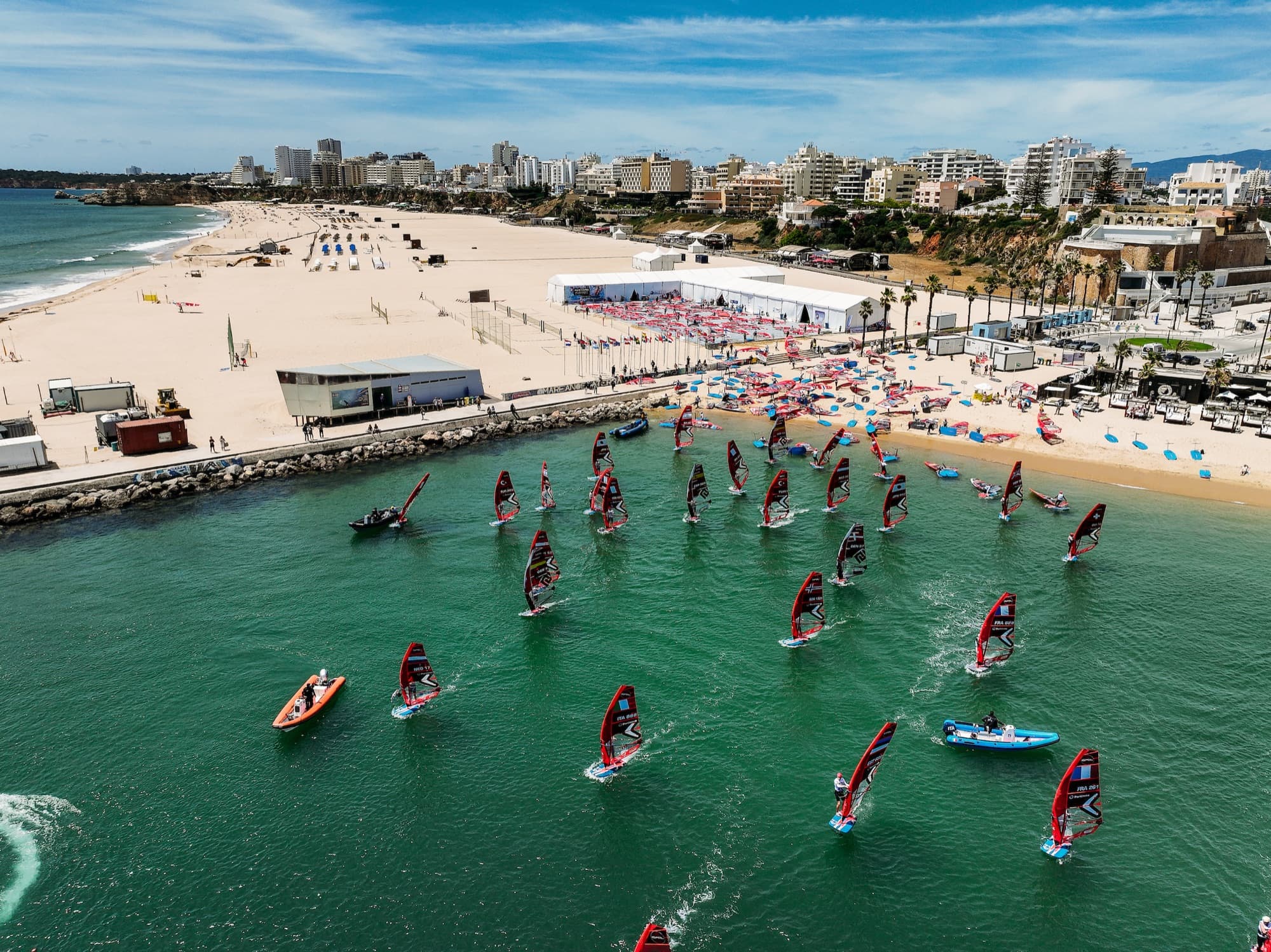 Luftaufnahme des Reviers: das Zeltlager und der Materialplatz an der Praia da Rocha, davor das Feld auf dem grünen Wasser