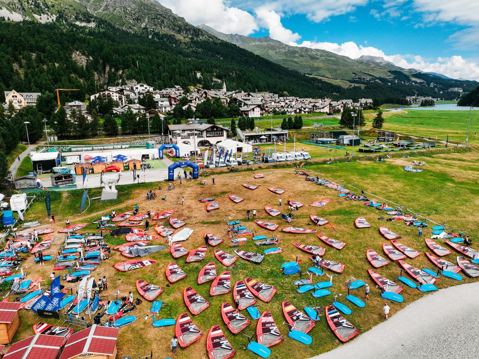 Luftaufnahme des Reviers: Boat Park auf der Wiese am Silvaplanersee, dahinter das Dorf und die Berge