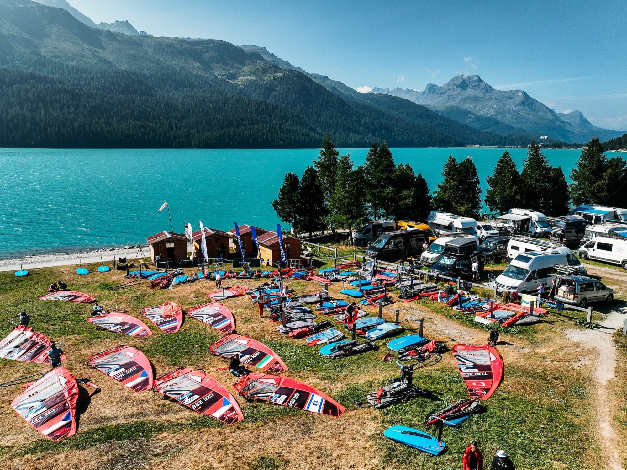 Luftaufnahme des Boat Parks am Ufer: Segel und Boards auf der Wiese, daneben die Wohnmobile der Teams