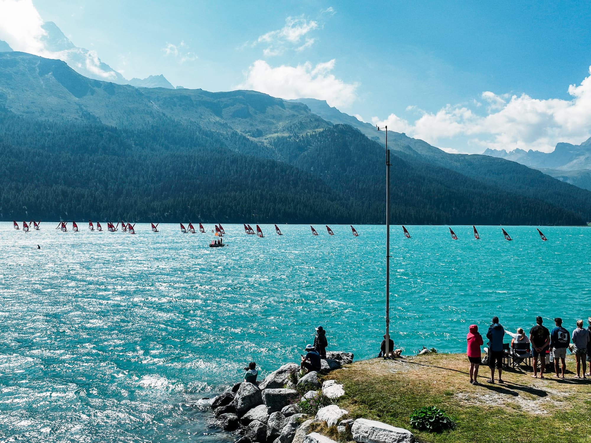 Zuschauerinnen und Zuschauer auf den Ufersteinen verfolgen das Feld weit draussen auf dem See